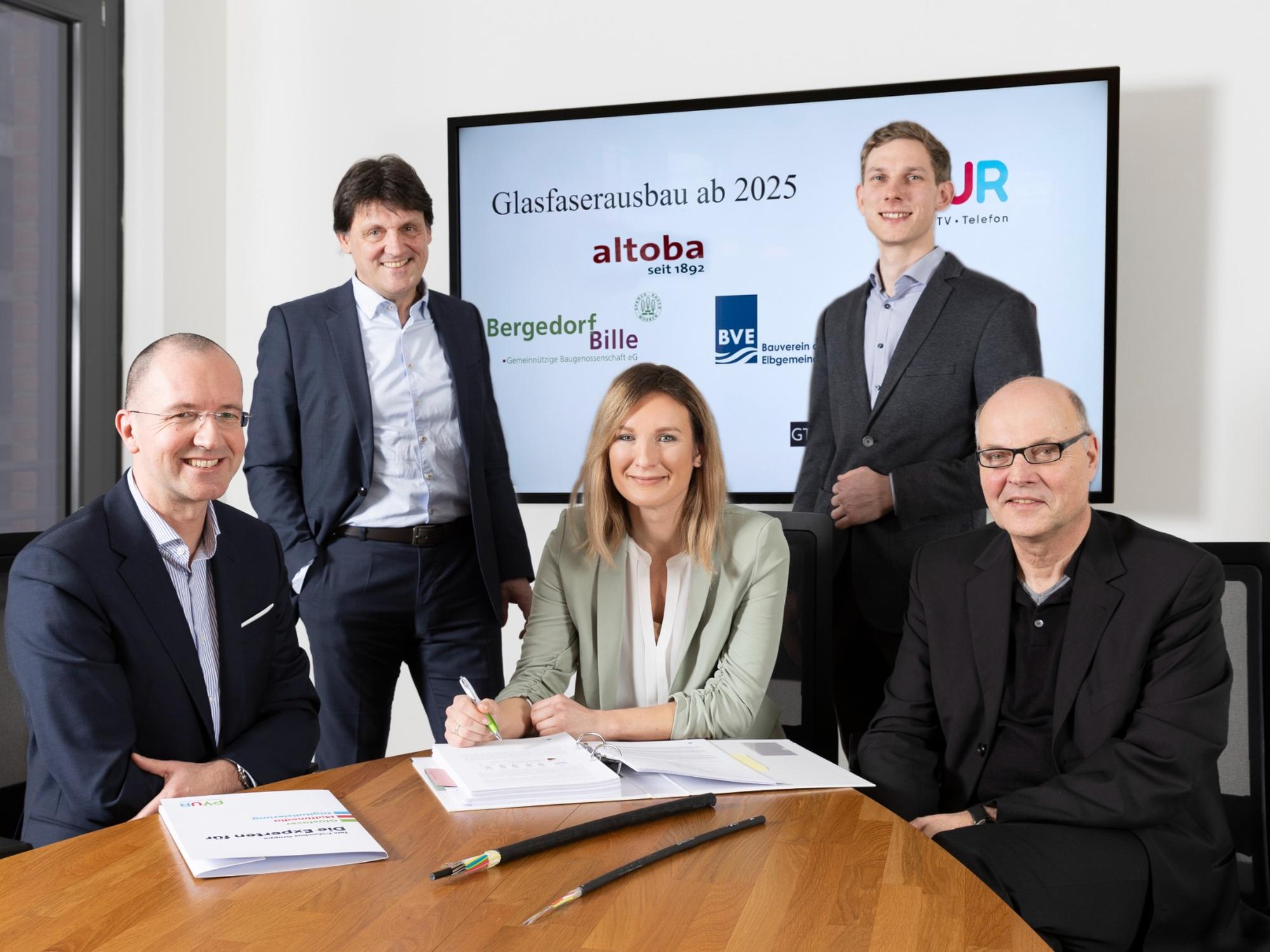Fünf Personen in Businesskleidung sitzen und stehen an einem Konferenztisch vor einem Bildschirm mit der Aufschrift „Glasfaserausbau ab 2025“ und den Logos von altoba, Bergedorf-Bille, BVE und PŸUR; auf dem Tisch liegen Vertragsunterlagen und ein aufgeschnittener Glasfaserkabelstrang, in der Mitte unterschreibt eine Frau ein Dokument.
